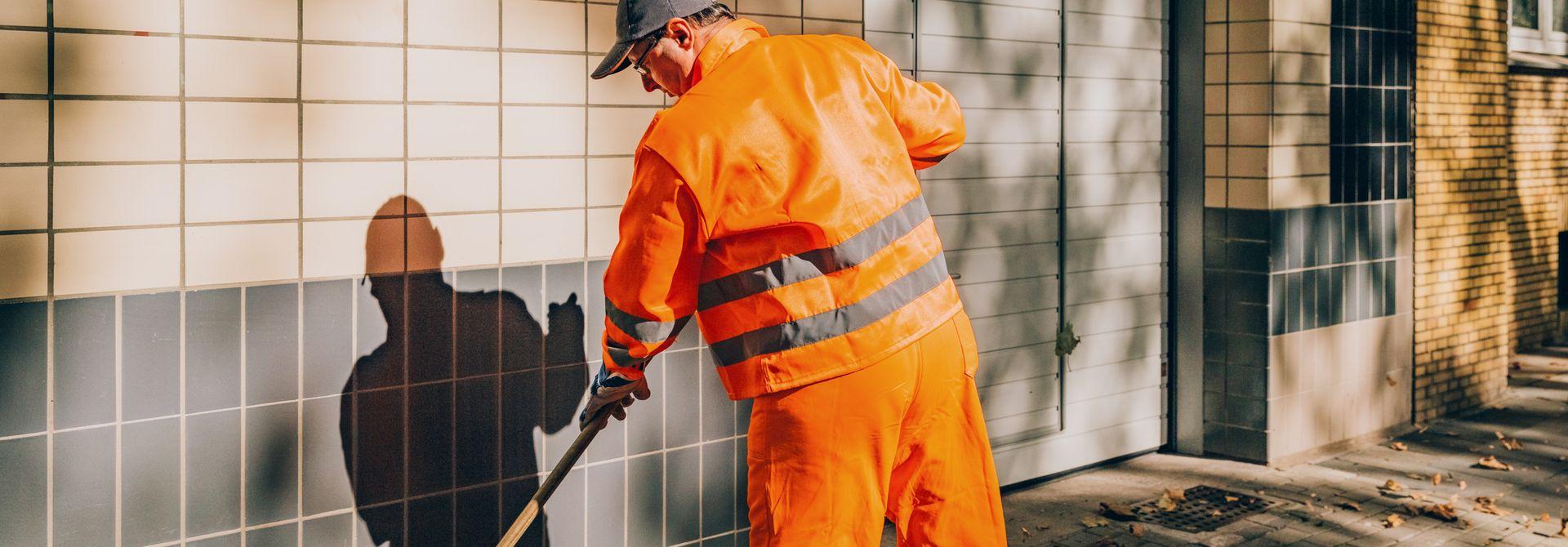 Mann in oranger Arbeitskleidung fegt mit einem Besen