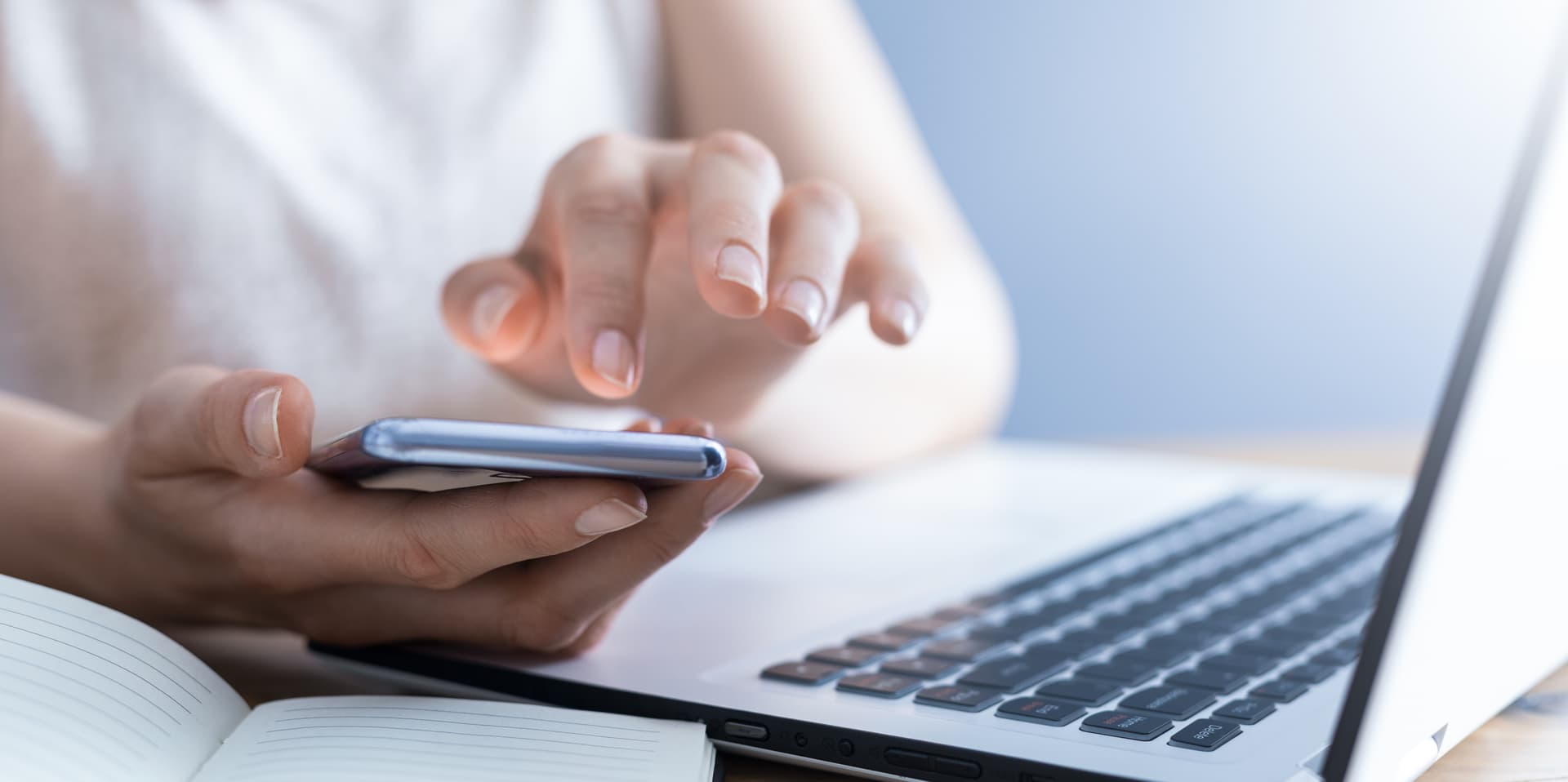Frau hält Smartphone in der Hand, davor liegen ein Notebook und ein Heft