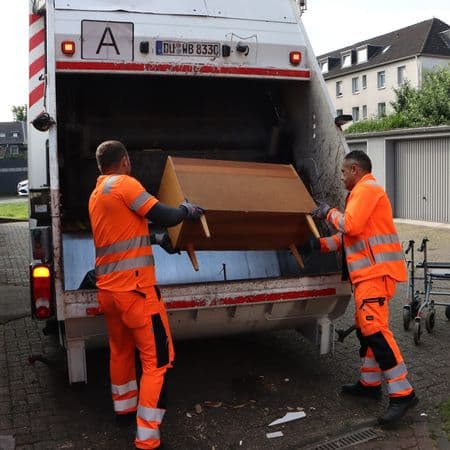 Müllwerker werfen Kommode in Sperrgutwagen