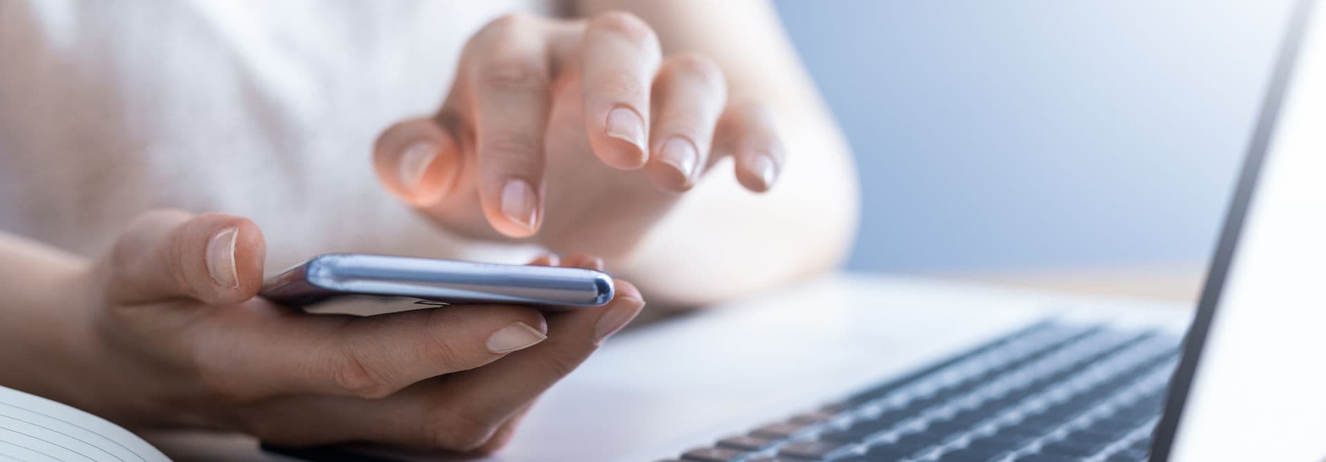 Online-Abfallkalender Frau hält Smartphone in der Hand, davor liegen ein Notebook und ein Heft